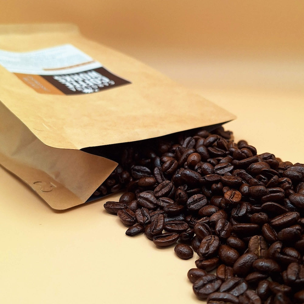 Whole specialty coffee beans pouring out of a Carolina Coffee Works bag.