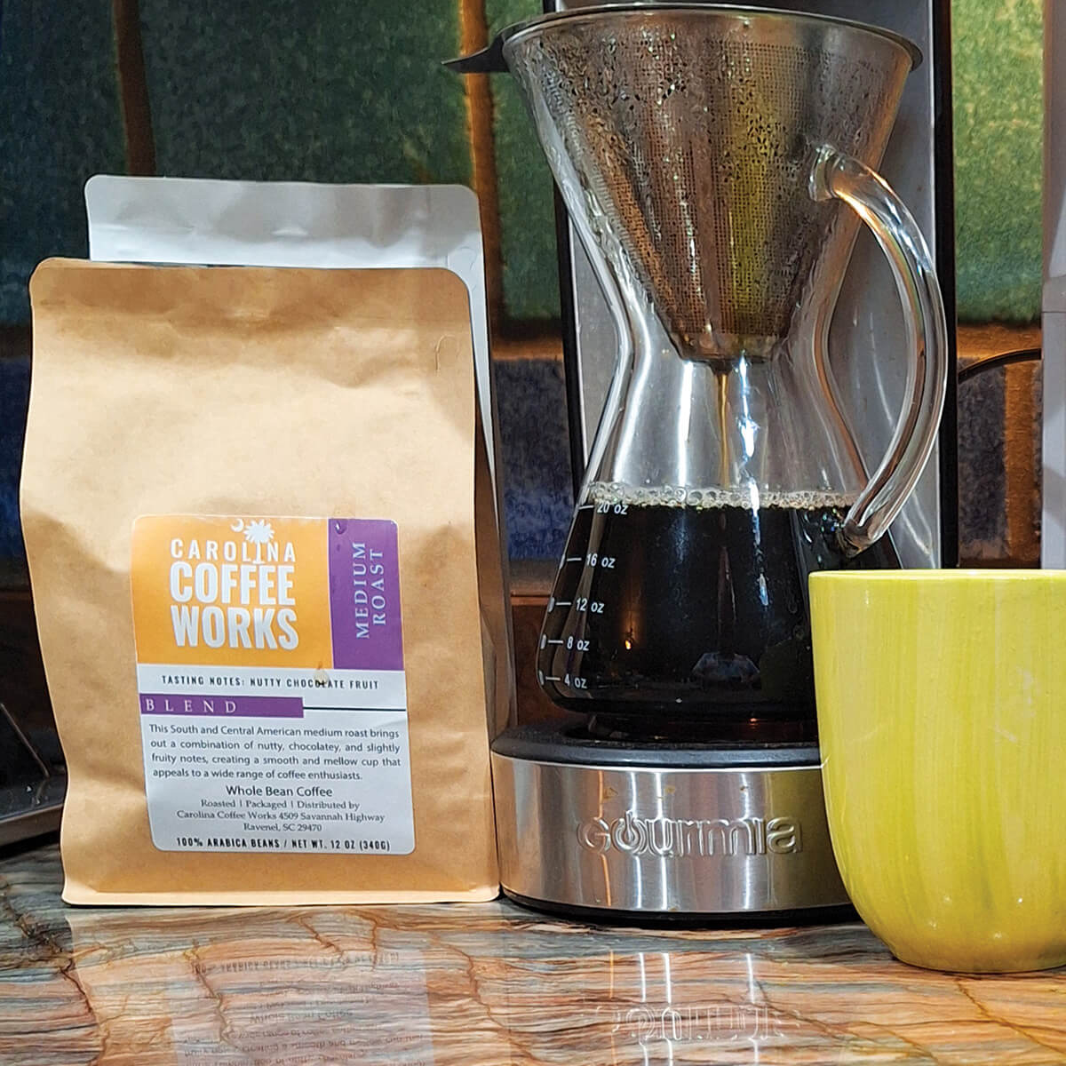 A bag of Carolina Coffee Works medium roast coffee on a kitchen counter, next to a pot of coffee and a bright green mug.