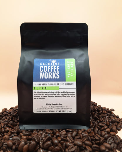 A black bag of Carolina Coffee Works west coast espresso sitting on a pile of dark roasted coffee beans.